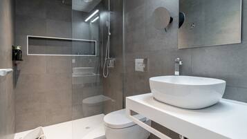Un baño moderno con un lavamanos grande de color blanco, una cabina de ducha de vidrio y un inodoro.