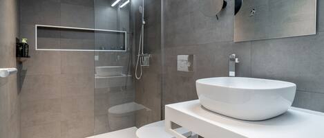 Un baño moderno con un lavamanos grande de color blanco, una cabina de ducha de vidrio y un inodoro.