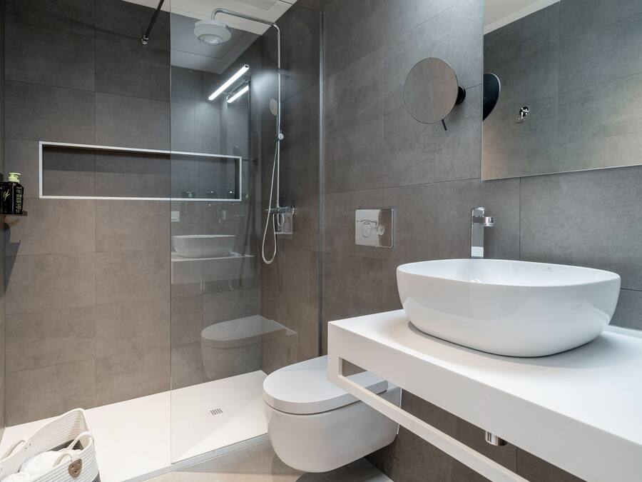 Un baño moderno con un lavamanos grande de color blanco, una cabina de ducha de vidrio y un inodoro.