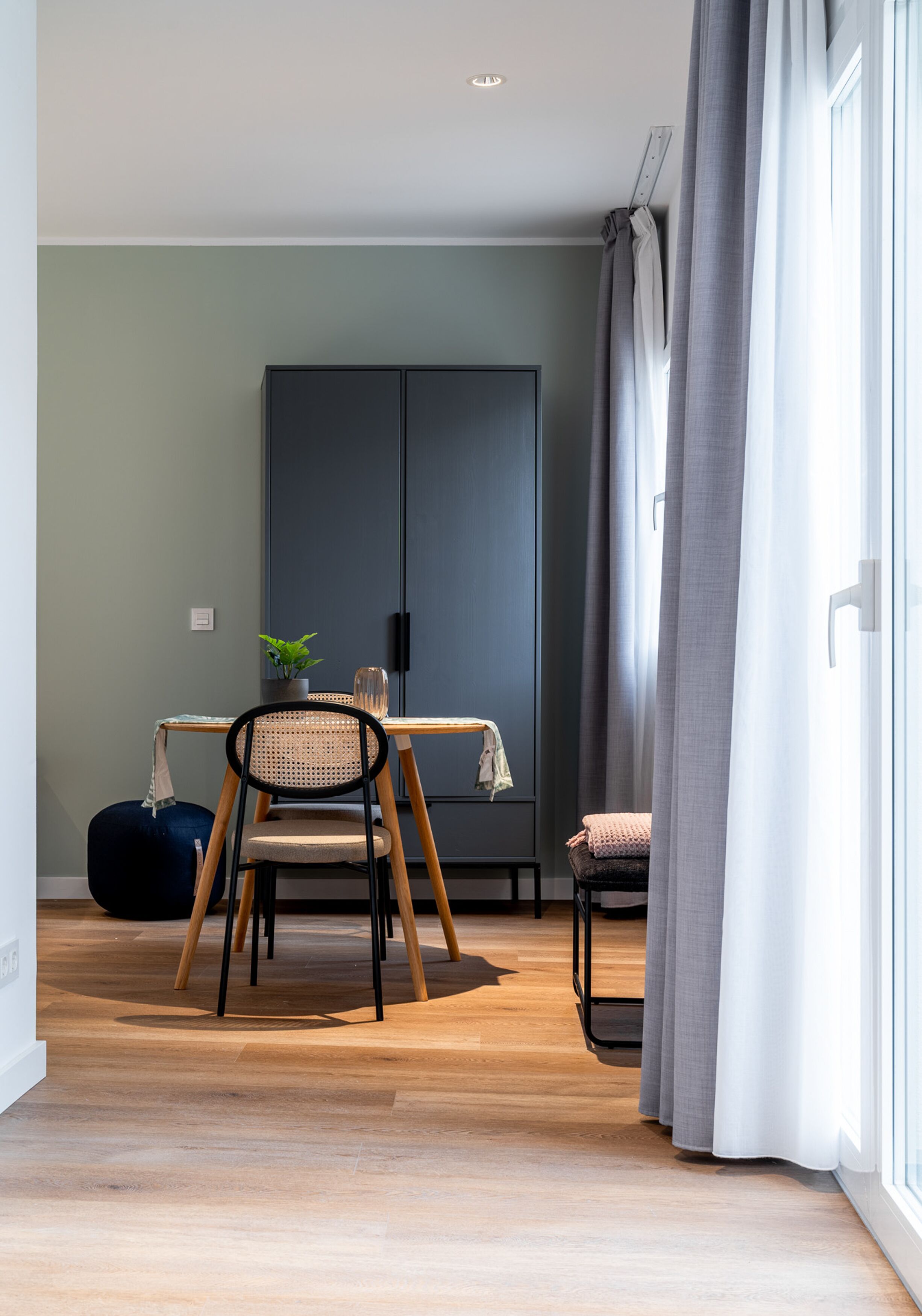 Un salon moderne avec un plancher en bois, une table à manger, une chaise noire, un fauteuil en forme de poire bleu et une armoire grise.