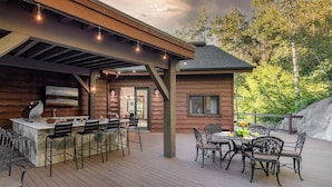 A wooden cabin with a deck, outdoor seating, and a bar area.