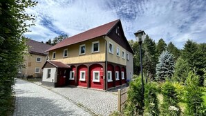 En tvåvåningsbyggnad med en röd och gul fasad, en uppfart belagd med kullersten och en gatlykta.