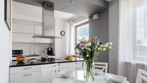 A modern kitchen with white cabinets, a black countertop, and a dining table set for four. - Bagno (Warsaw)