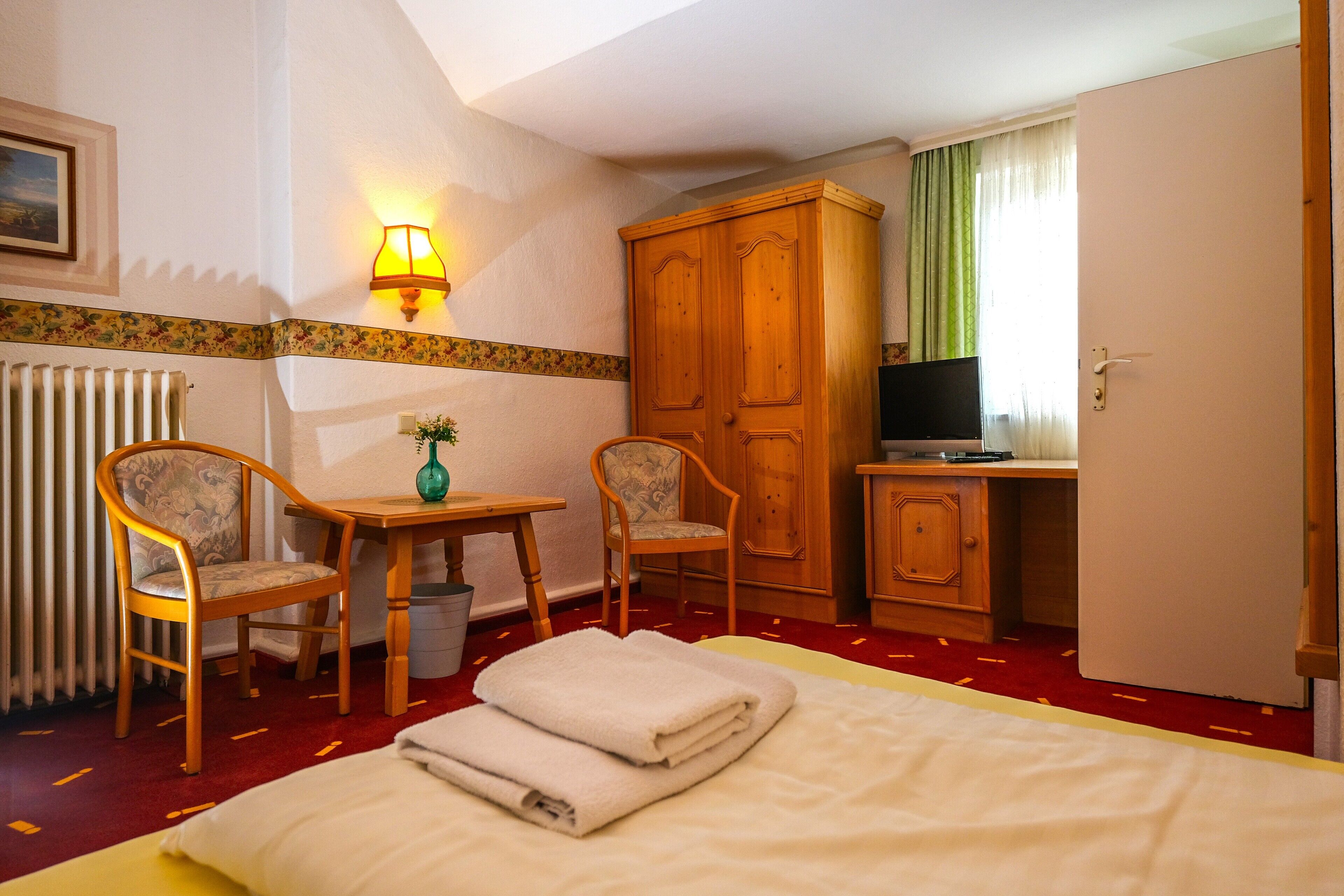 Hotelkamer met een bed, twee stoelen, een tafeltje, een televisie en een kledingkast.