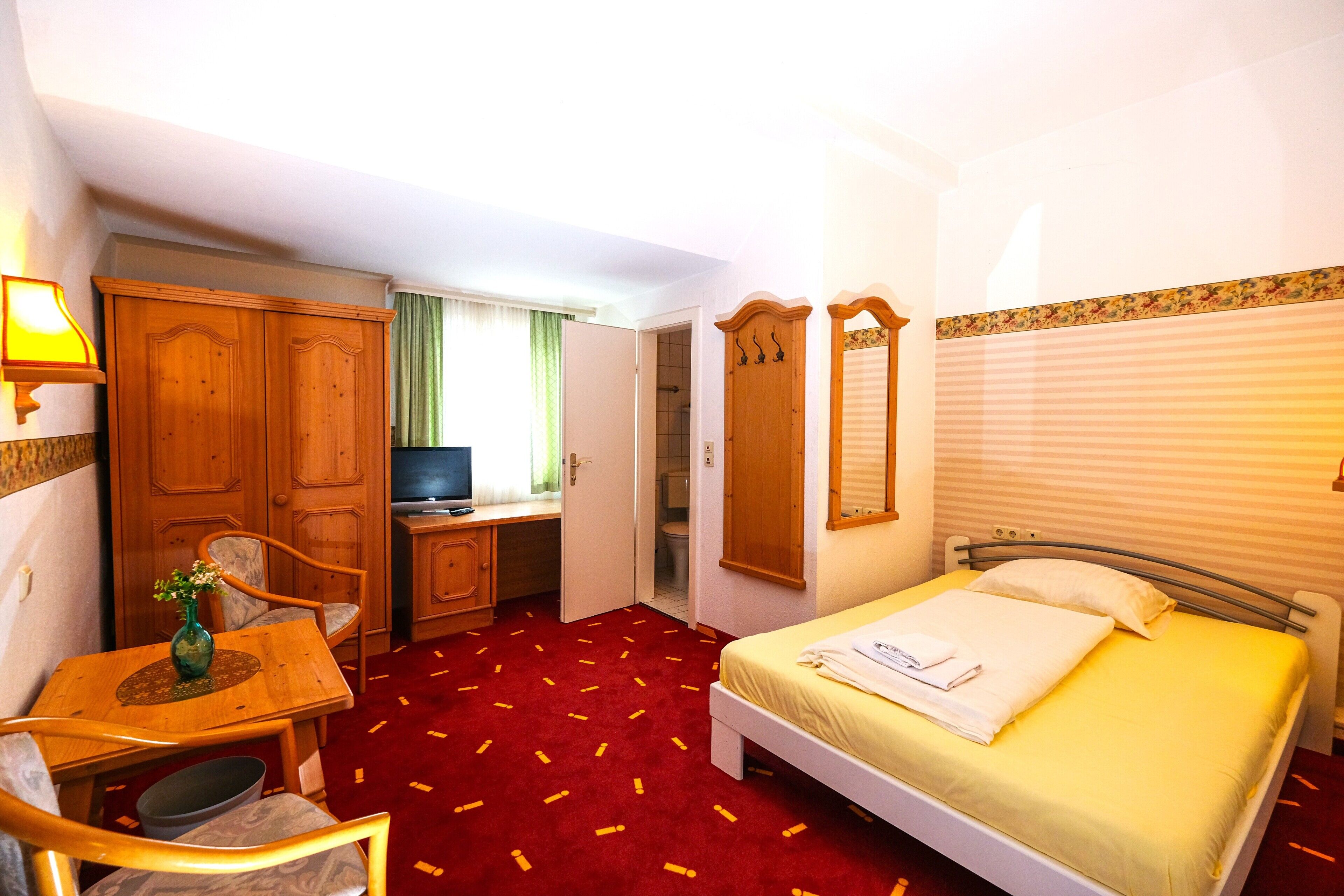 Una habitación de hotel con cama, escritorio, silla, televisor y armario.
