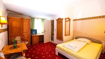 Una habitación de hotel con cama, escritorio, silla, televisor y armario.