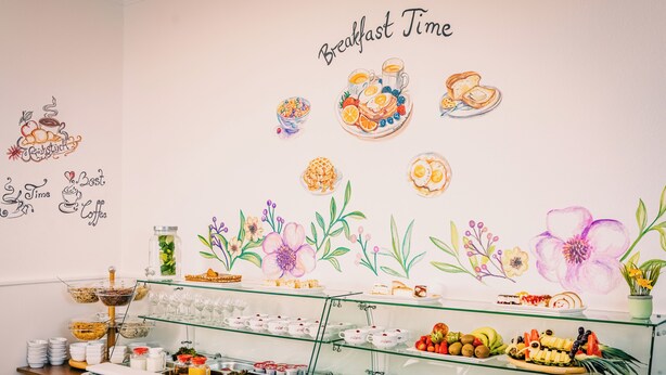 A breakfast buffet with various food items and a wall decorated with floral illustrations and the words "Breakfast Time". - Hotel Haus Am Walde (Bad Fallingbostel)
