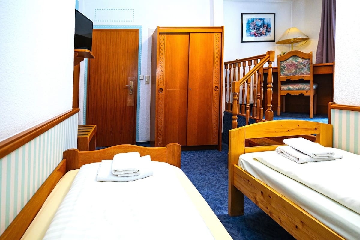 Quarto de hotel com duas camas de madeira, um guarda-roupa de madeira, uma cadeira e uma escada.