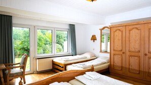 A room with three wooden beds, a wooden wardrobe, a chair, and a window with curtains. - Hotel Haus Am Walde (Bad Fallingbostel)