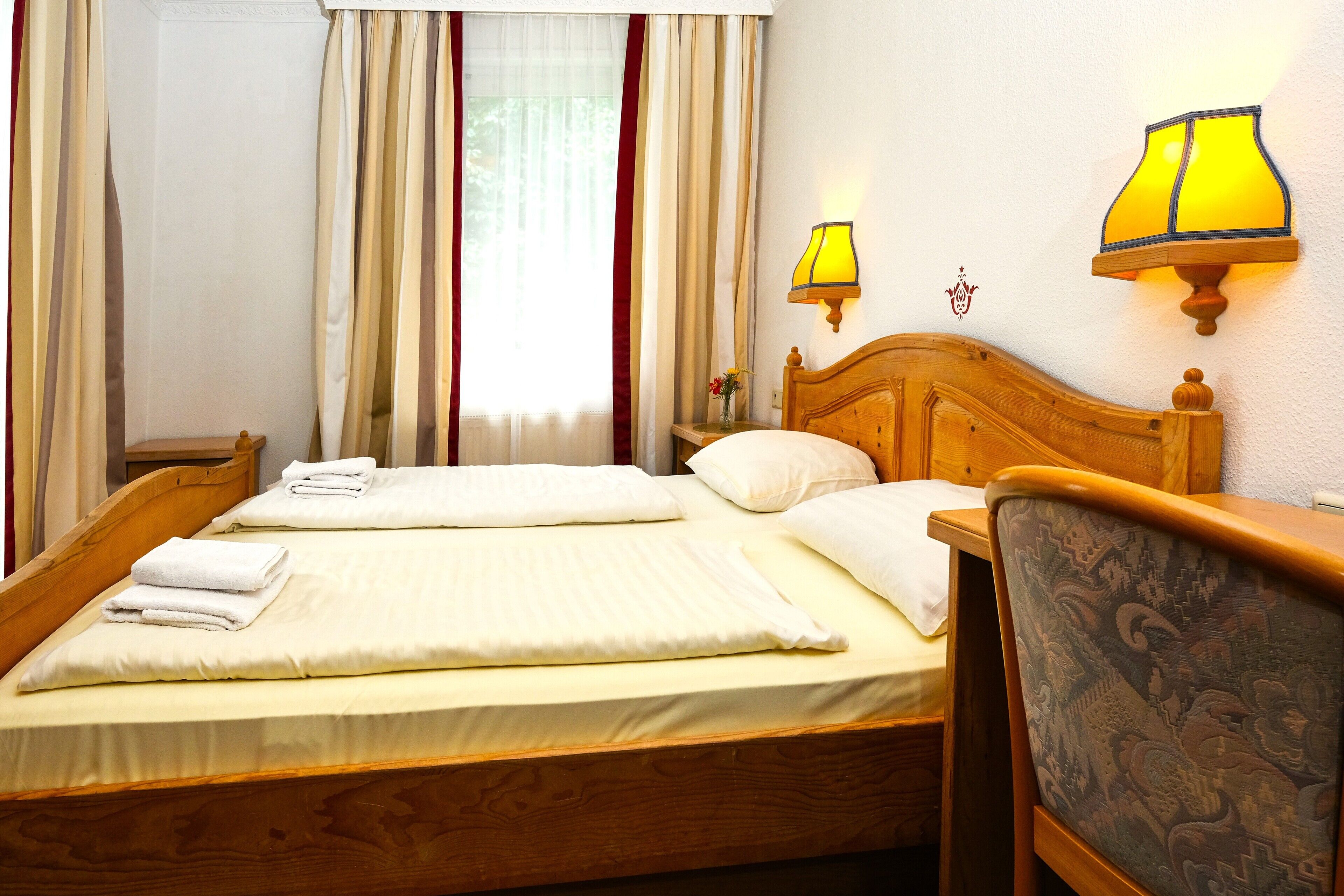 Un lit bien fait, avec des oreillers et des serviettes pliées, une tête de lit en bois et deux lampes fixées au mur.