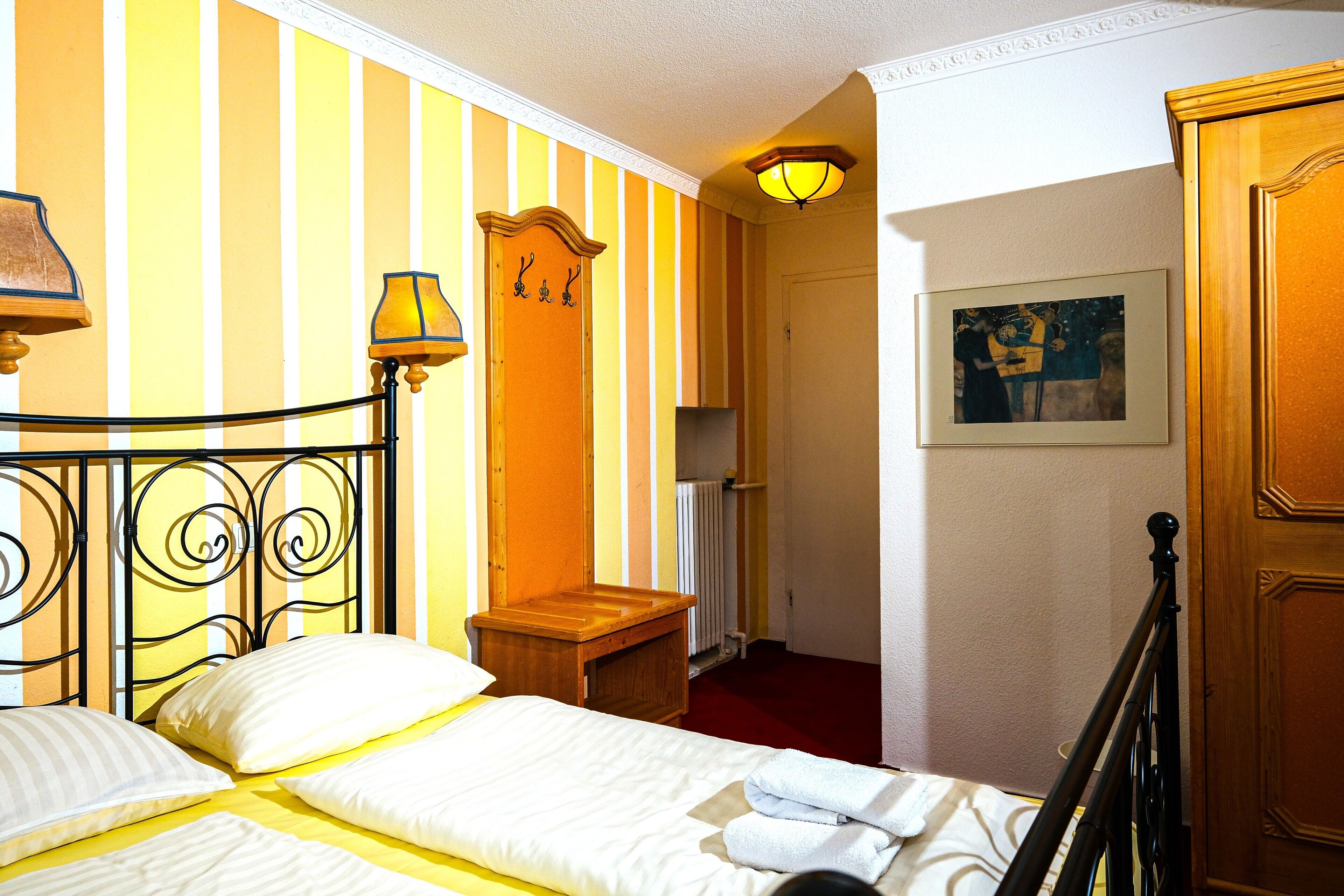 A hotel room with a bed, a nightstand, a wooden door, a radiator, and a painting on the wall.