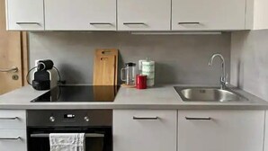 A kitchen with white cabinets, a black stove, a wooden cutting board, a red mug, and a stainless steel sink. - Brand New Apartments 4.1 (Hlavní mesto Praha)