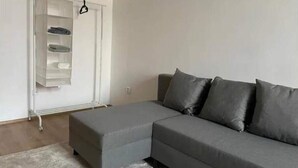 A living room with a grey sectional sofa, a white shelving unit, and a grey rug. - Brand New Apartments 4.1 (Hlavní mesto Praha)