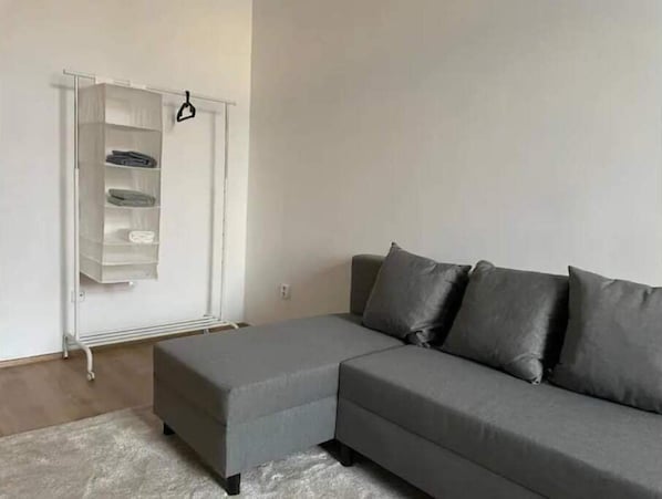 Un salon avec un canapé d’angle gris, une étagère blanche et un tapis gris.