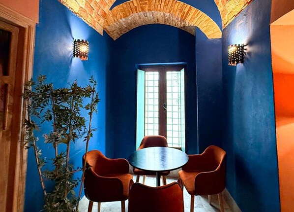 A room with a blue wall, a wooden ceiling, a round table with four chairs, and a window with a grid pattern.