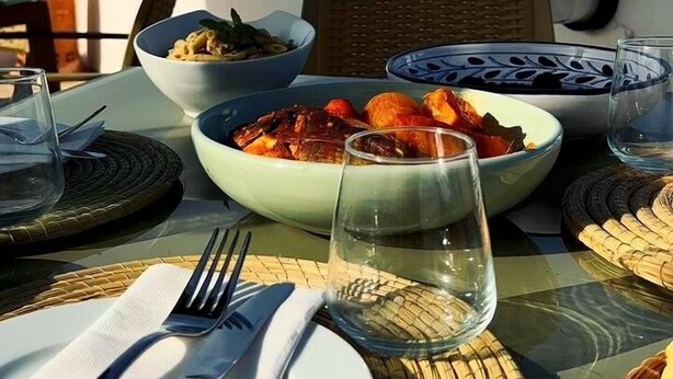 Mesa lista para una comida, con platos y vasos, con vistas a un paisaje urbano.