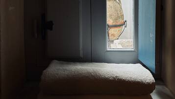 Una habitación con una puerta que da a un ventanal pequeño, un banco blanco acolchado y una planta en maceta afuera.