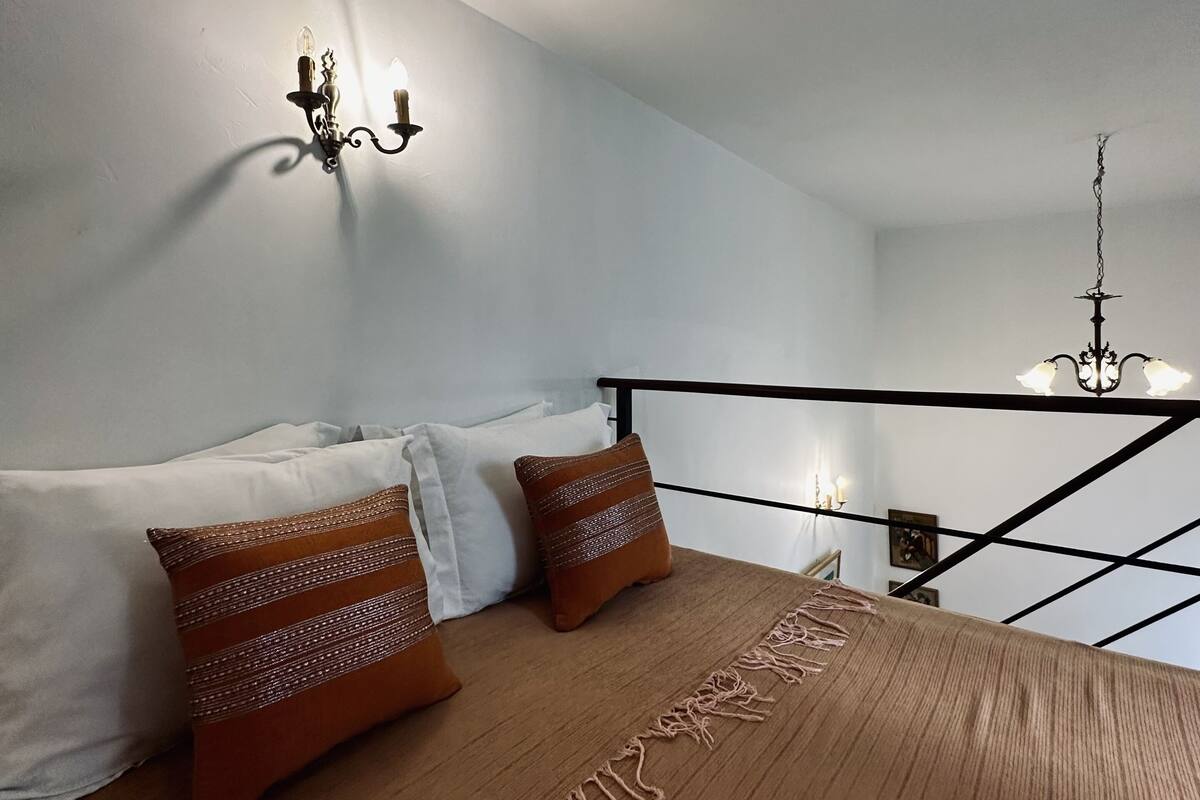A bedroom with a bed, pillows, a wall-mounted light fixture, and a chandelier.