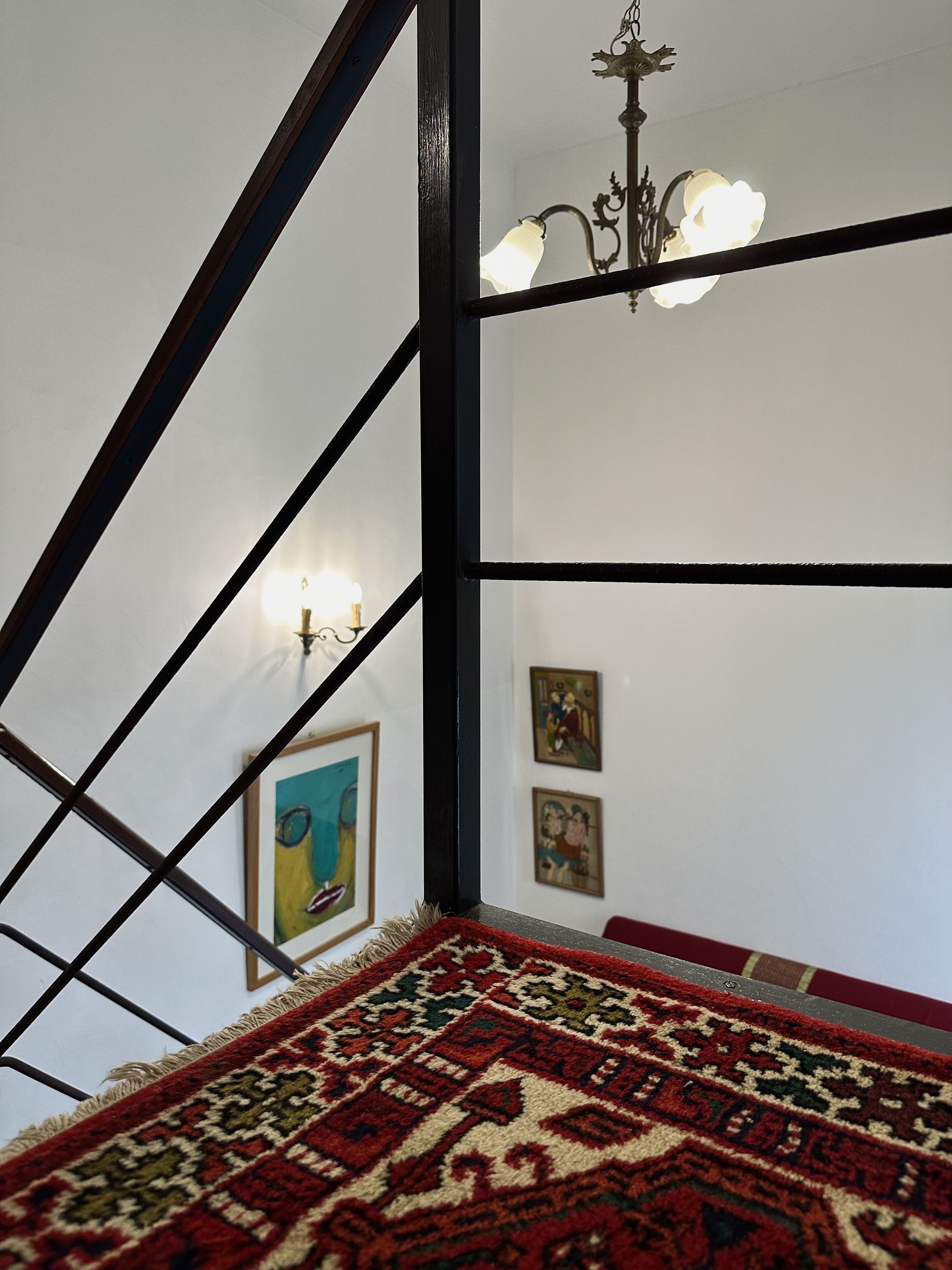 A staircase with a patterned carpet, a chandelier, and framed artwork on the walls.