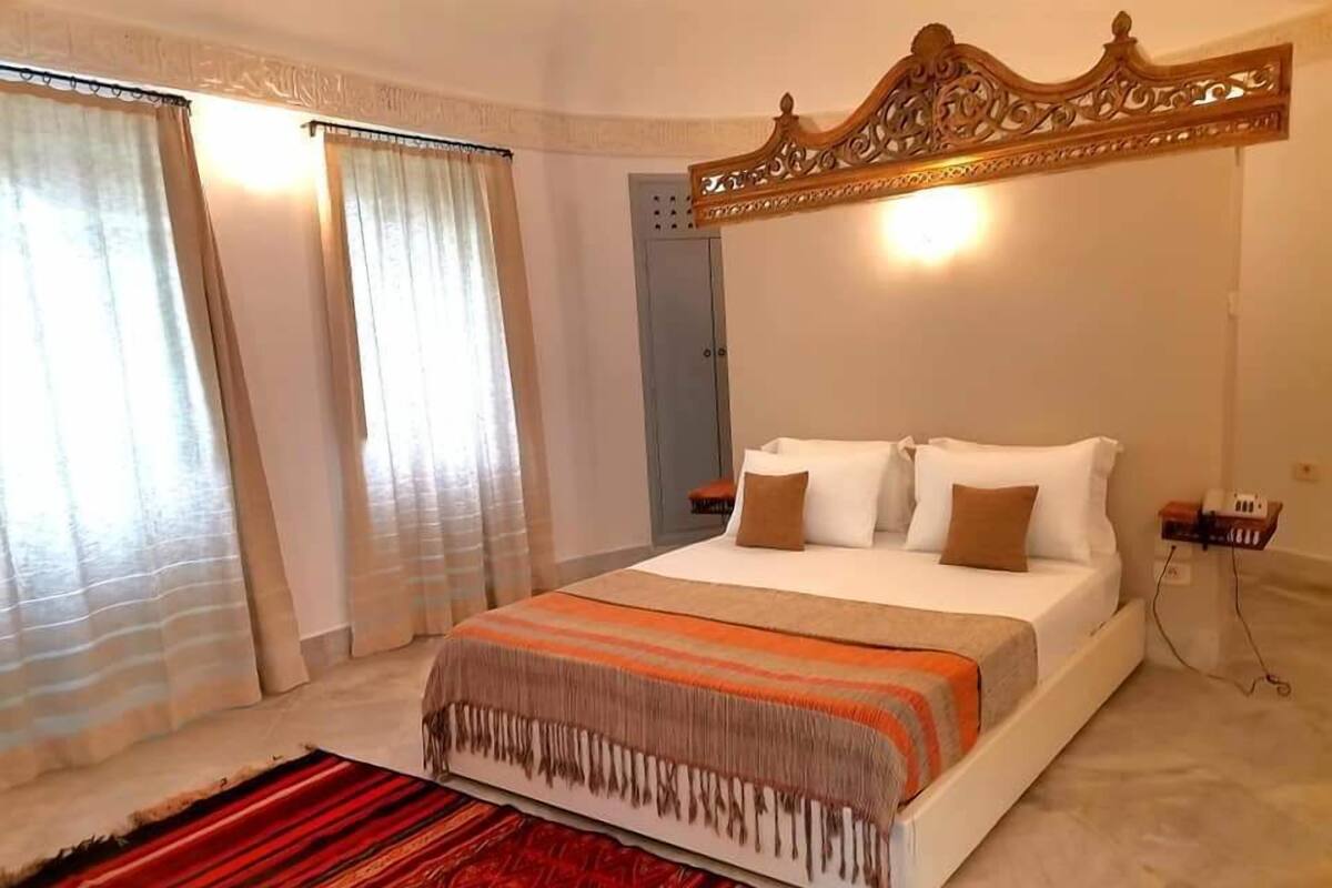 A hotel room with a large bed, a wooden headboard, and a red patterned rug.