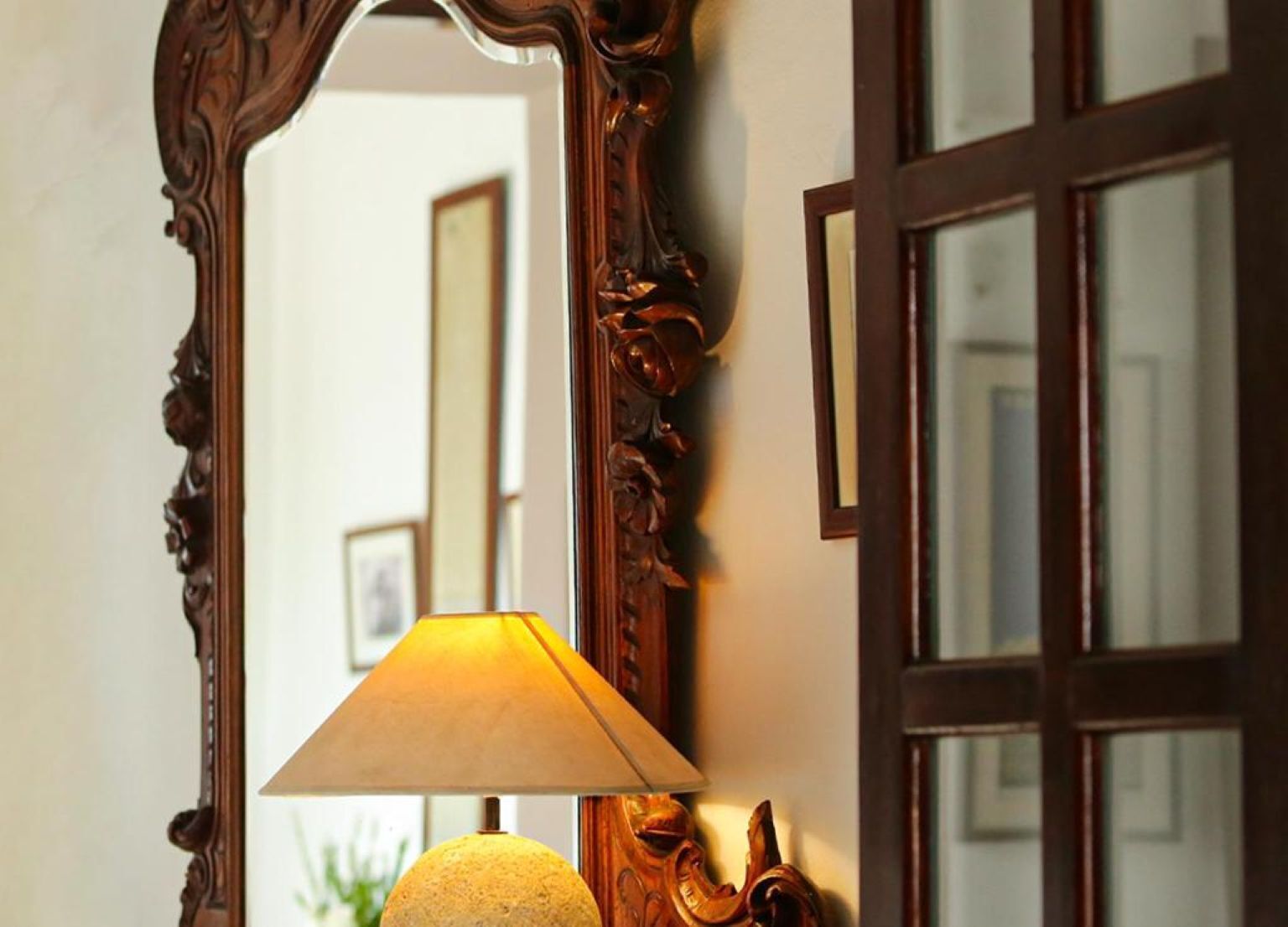 A mirror with an ornate wooden frame, a lamp with a beige shade, and a window with multiple panes.
