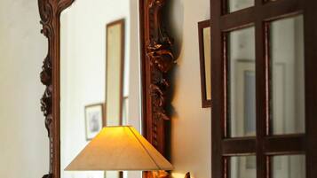 A mirror with an ornate wooden frame, a lamp with a beige shade, and a window with multiple panes.