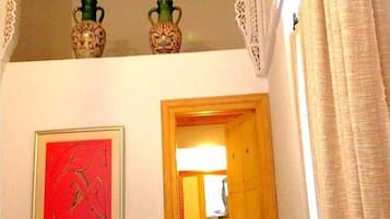 Una habitación con un cuadro abstracto enmarcados, una puerta de madera que da a otra estancia, y dos jarrones decorativos en el techo.