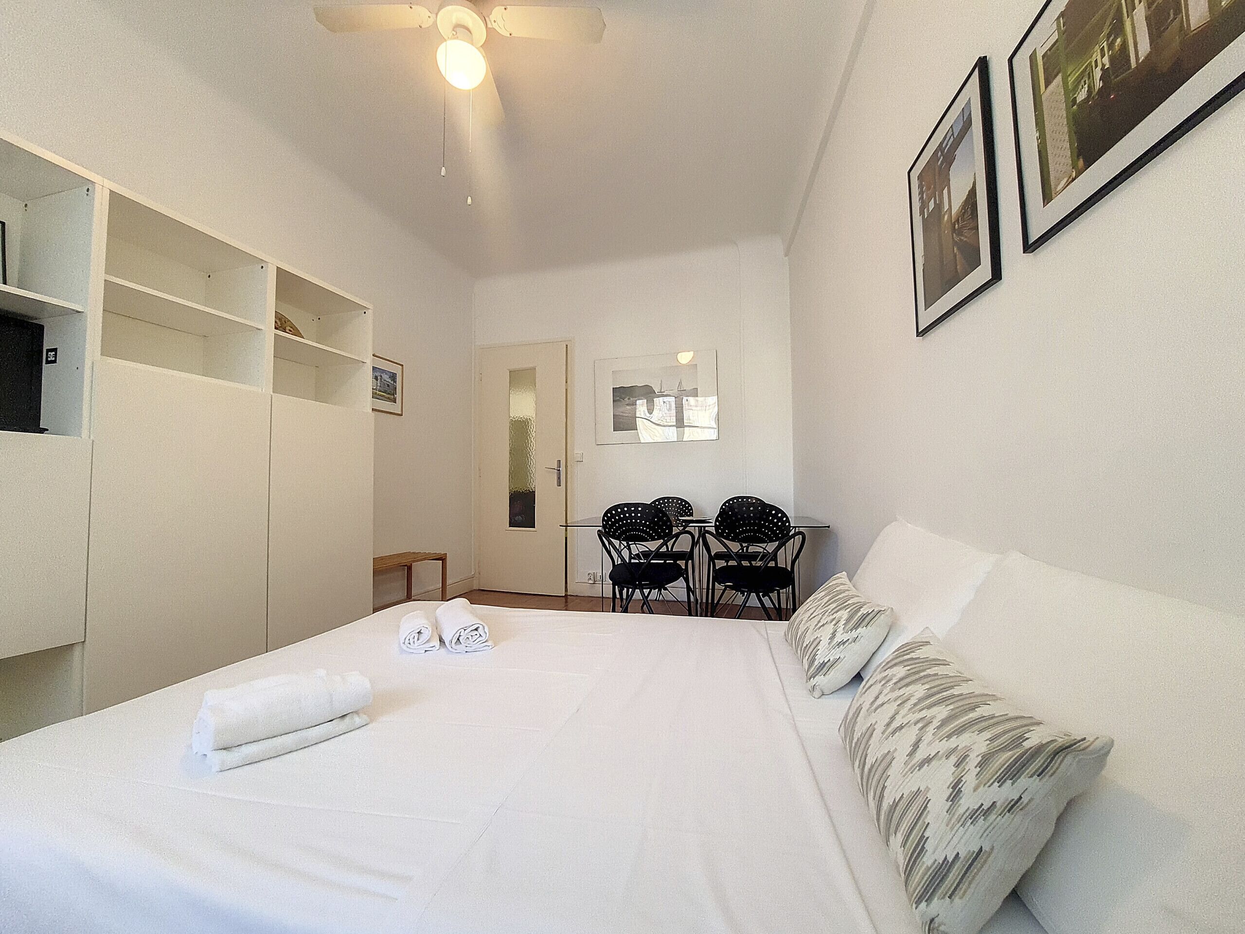 Quarto com cama, ventoinha no teto, escrivaninha, duas cadeiras e espelho.