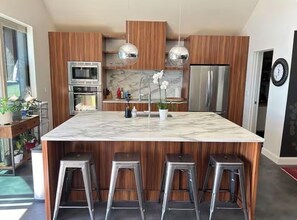 A modern kitchen with a large island, stainless steel appliances, wooden cabinetry, and bar stools.