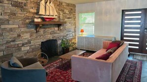 A living room with a stone wall, a fireplace, a sofa, a chair, and a patterned rug.