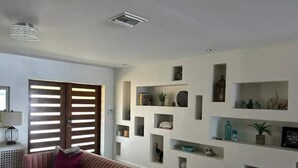 A living room with a sofa, a wall-mounted shelf with decorative items, and a door with horizontal slats.