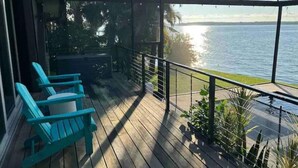 A wooden deck with a covered area, a view of the water, and a row of blue chairs.