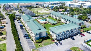 Vista aérea de un complejo hotelero frente al mar, con varias construcciones, zonas de estacionamiento y vistas al océano.