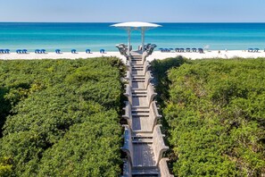 A wooden boardwalk leading to a beach with umbrellas and lounge chairs.