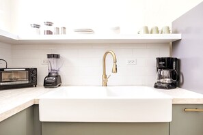 A kitchen with a white sink, a gold faucet, a black toaster, a blender, and a coffee maker. - 4 bedroom Miramar - 2 apt combo (San Juan)