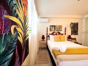A hotel room with a bed, a nightstand, a lamp, and a wall-mounted air conditioner.