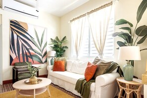 Un salon avec un canapé blanc, une table basse ronde et une grande plante.