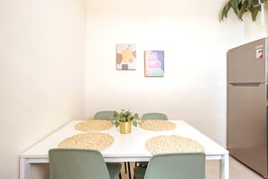 A dining area with a white table, four chairs, and two wall-mounted artworks. - 4 bedroom Miramar - 2 apt combo (San Juan)