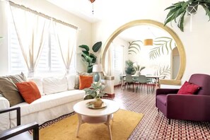 A living room with a white sofa, a round coffee table, and a purple armchair. There is a large mirror on the wall and a dining area in the background. - 4 bedroom Miramar - 2 apt combo (San Juan)