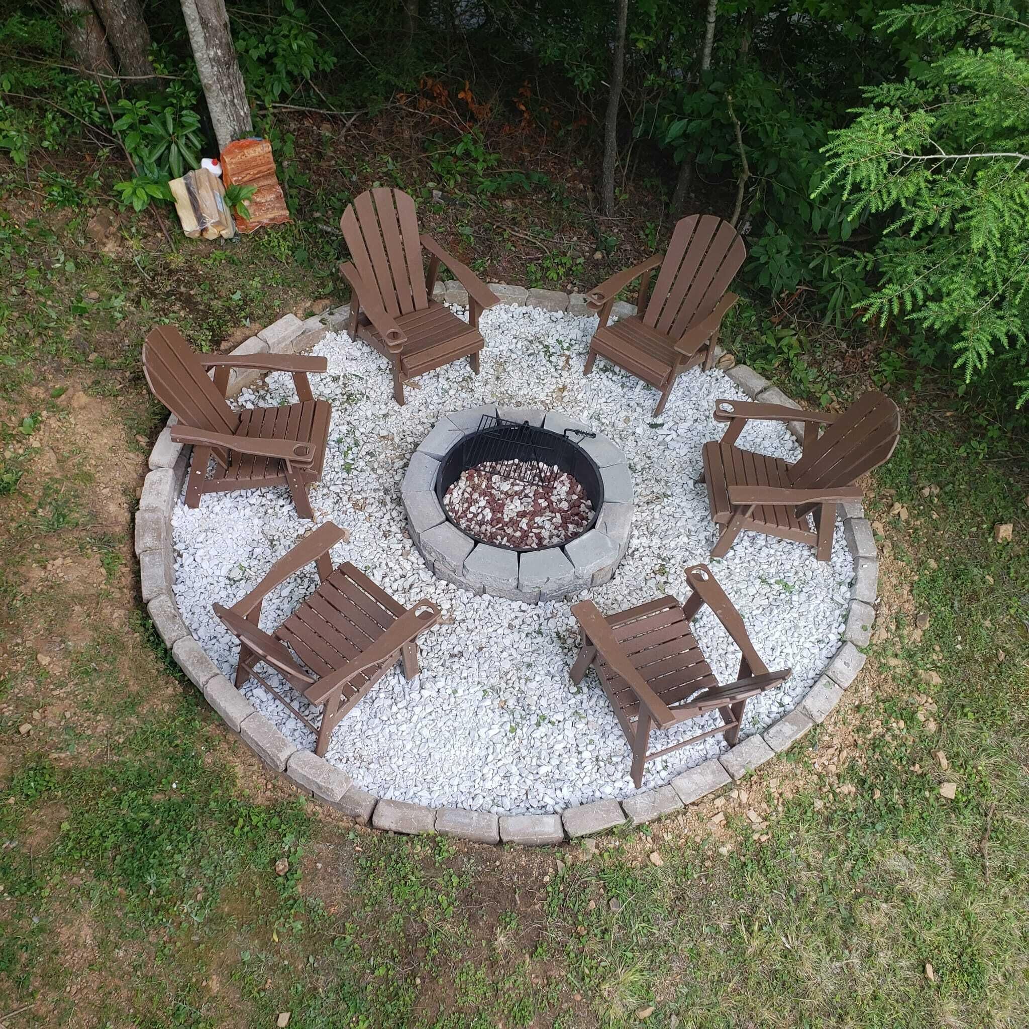 A circular outdoor seating area with six Adirondack chairs around a stone fire pit.