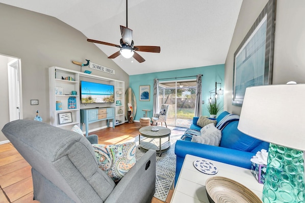 A living room with a blue sofa, grey armchair, and a TV on a white shelf.