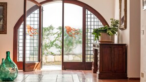 A room with a large arched doorway leading to a garden, a wooden cabinet, and a green vase on the floor. - Villa La Fenice by Wonderful Italy (Castellammare del Golfo)