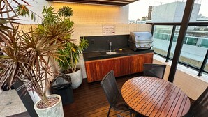 Eine Dachterrassenküche mit Grill, Holztisch, Stühlen und Topfpflanzen.