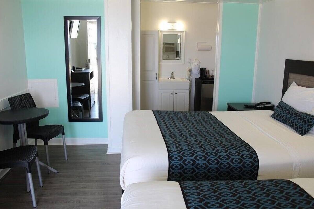 Una habitación de hotel con cama, escritorio, silla, espejo, lavamanos y armario.