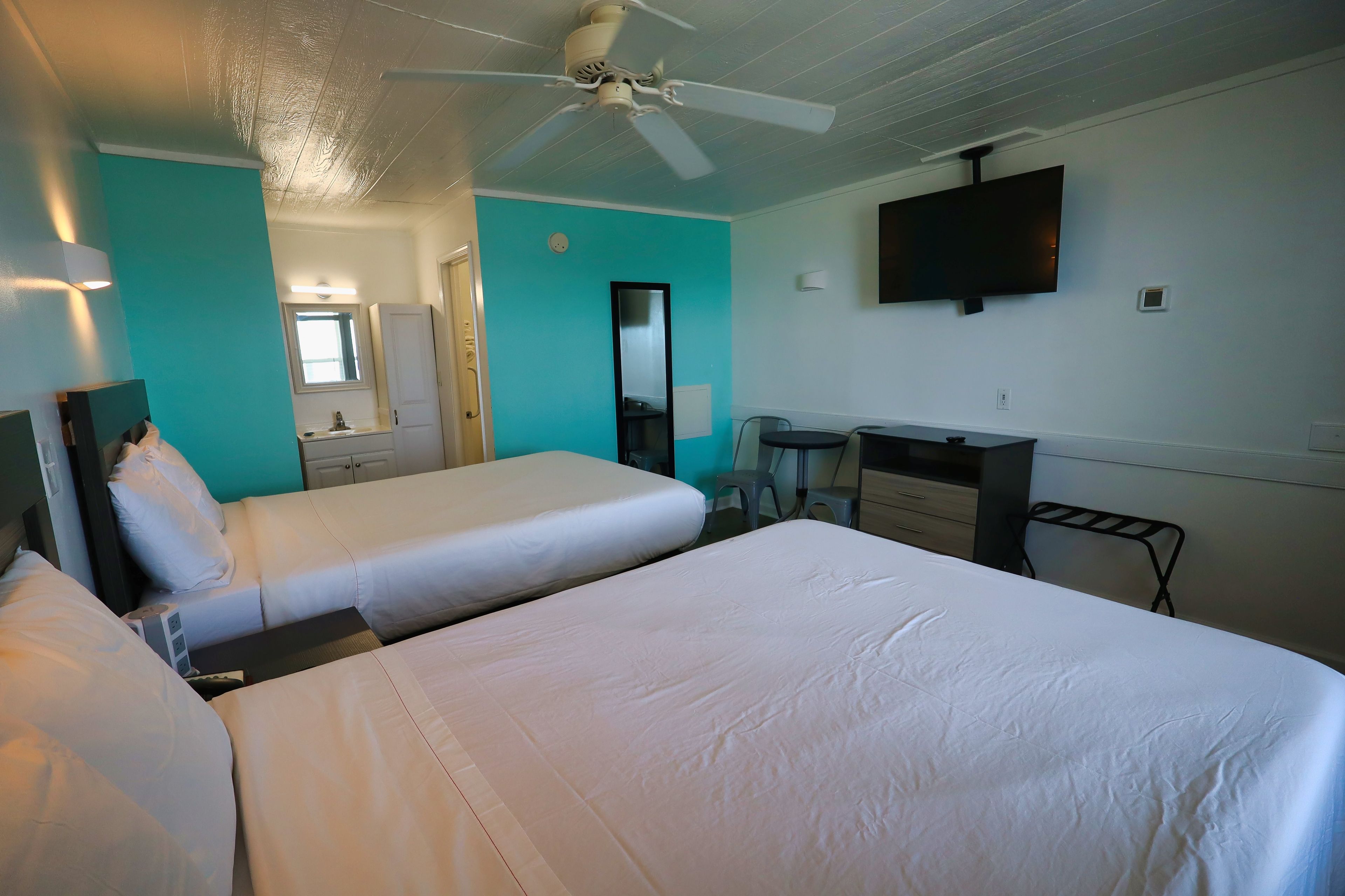 Une chambre d’hôtel avec deux lits, un bureau, une chaise, une télévision et un ventilateur de plafond.
