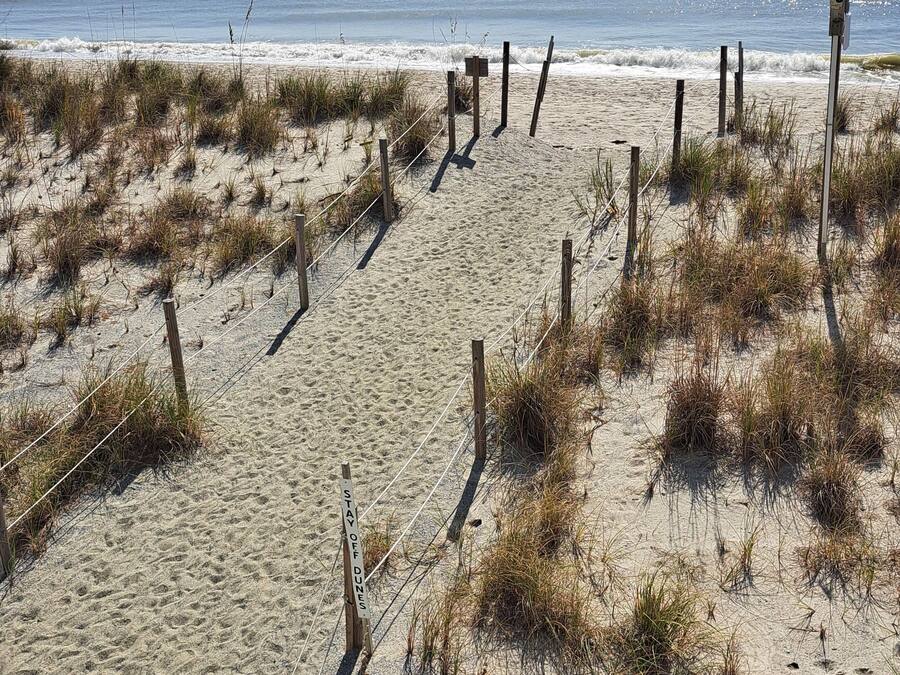 A sandy beach with a fence and a sign that reads "TAY OFF DUNES."