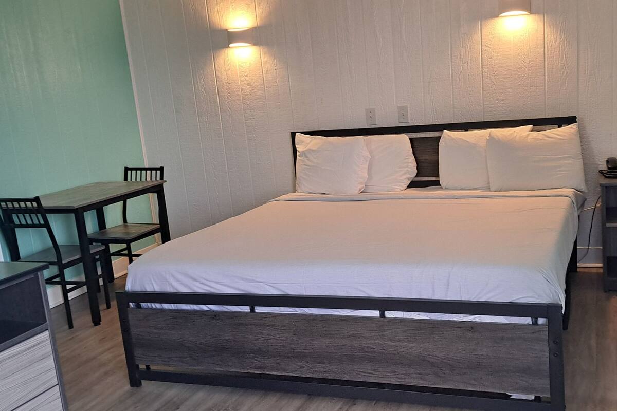 Un dormitorio ordenado con cama, mesita de noche y escritorio con sillas.