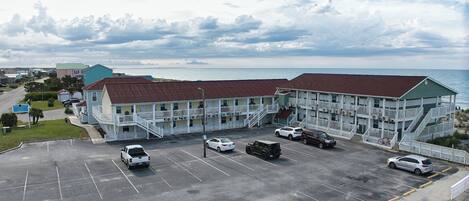 A motel with a parking lot, a beach view, and a large building with multiple balconies.
