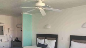 Une chambre d’hôtel avec deux lits, un ventilateur de plafond, une salle de bain avec douche et un téléphone sur la table de chevet.