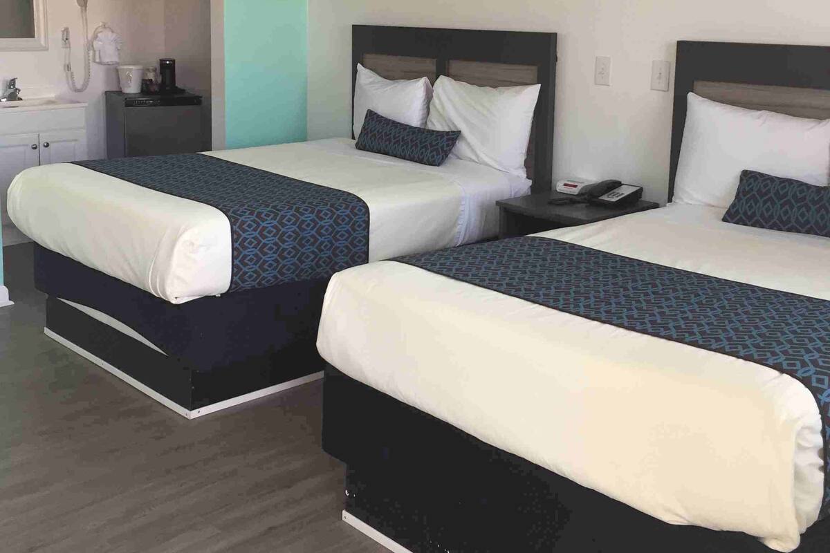 Habitación de hotel con dos camas, ventilador de techo, baño con ducha y teléfono en la mesita de noche.